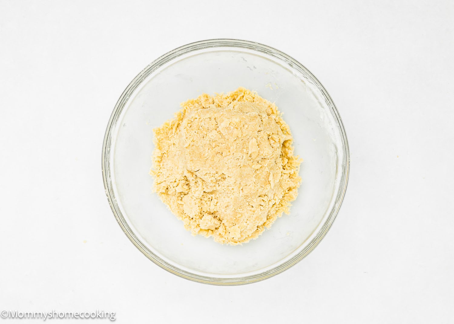 A glass bowl containing a light yellow dough, perfect for an easy press-in pie crust, sits on a white surface.