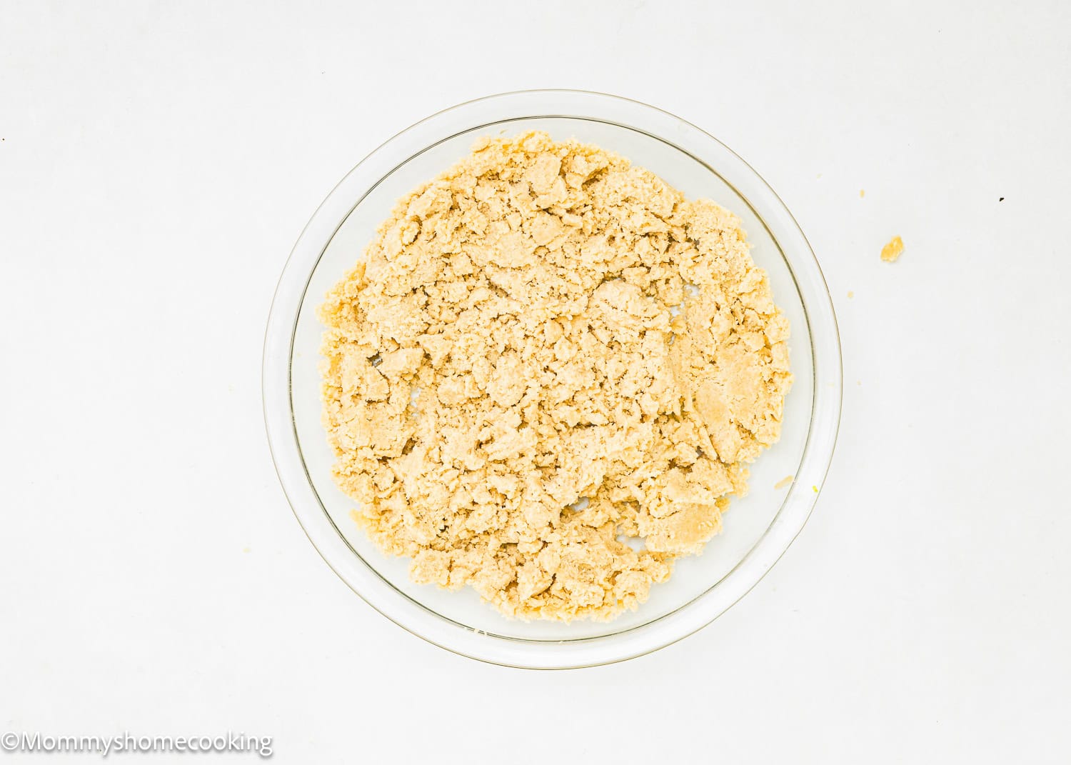 A glass bowl filled with crumbly dough mixture sits on a white surface, perfect for an easy, no-fuss pie crust that requires no chilling.