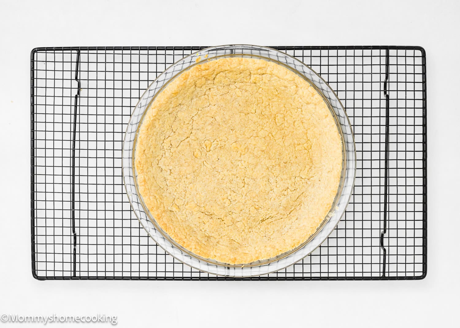 A no-fuss round pie crust sits in a glass dish on a black wire cooling rack, effortlessly set against a white background.