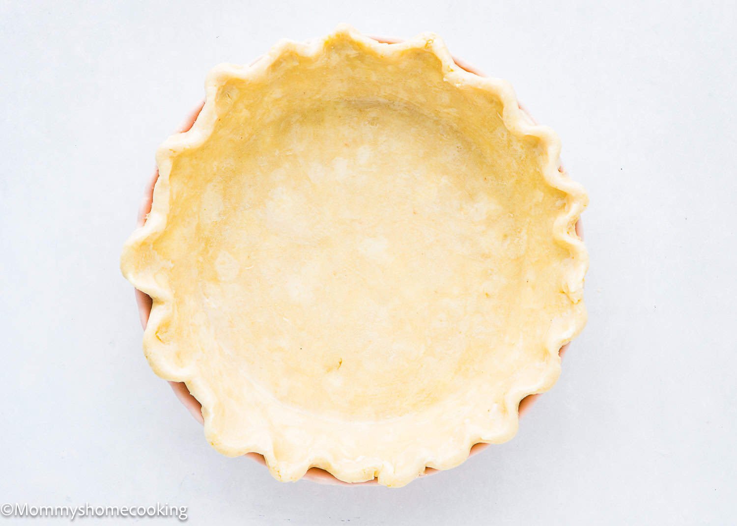 An unbaked eggless crust with crimped edges, all resting on a light surface.