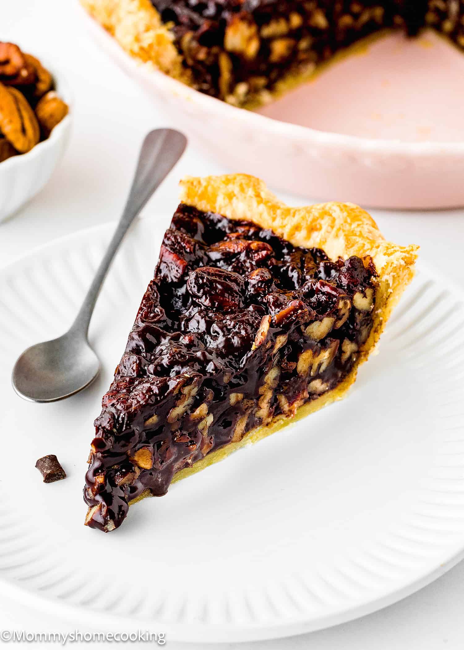 a slices of egg-free chocolate pecan pie in a plate with a spoon on the side. 