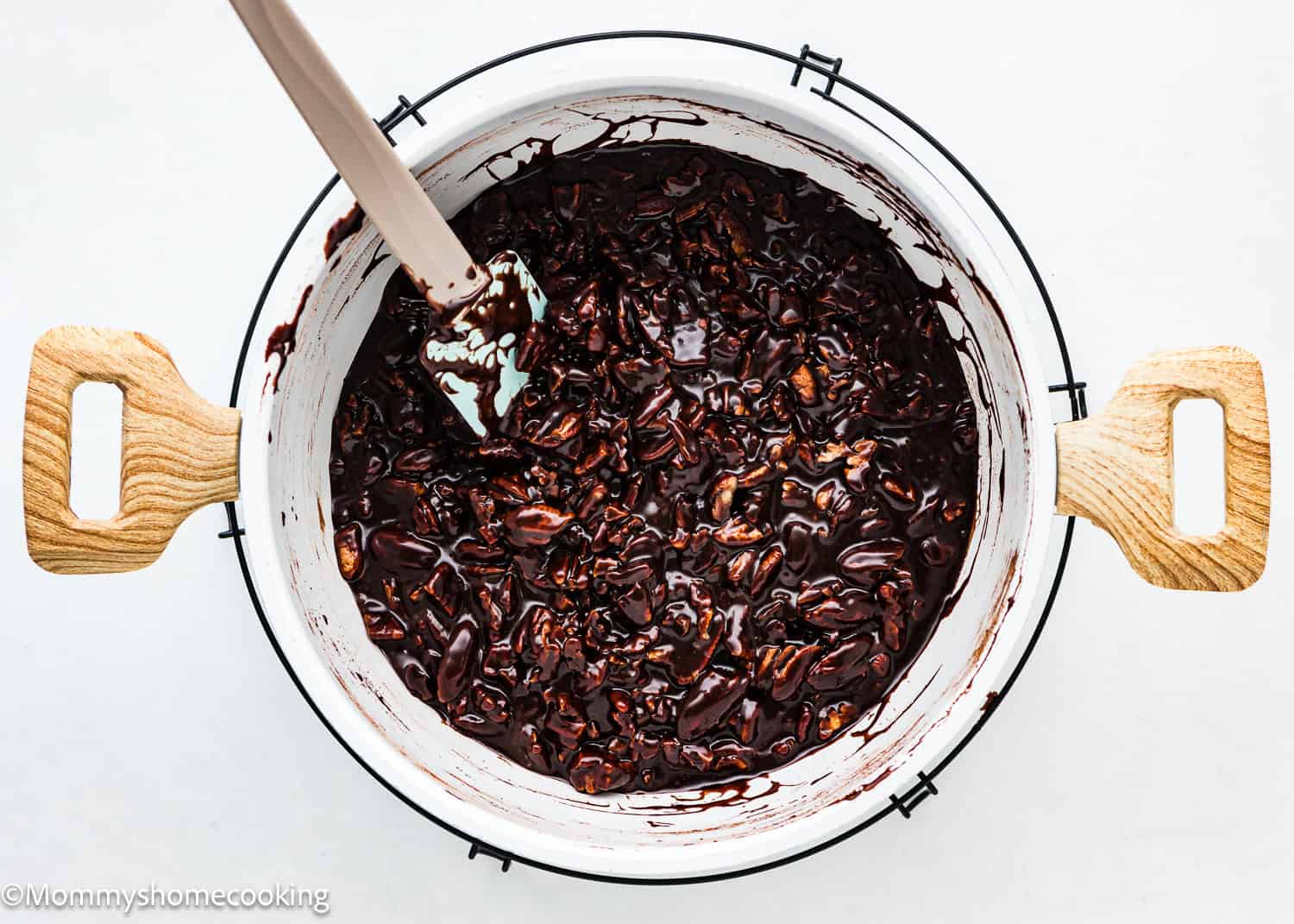 A pot filled with chocolate-covered nuts and a wooden spoon sits on a white background, reminiscent of the effortless charm of an eggless easy chocolate pecan pie.