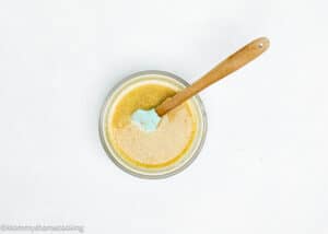 A glass bowl with a gold flaxseed mixture and a blue spatula with a wooden handle sits on a white surface, perfect for whipping up a batch of eggless pecan pie brownies.