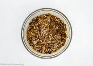 A glass bowl brimming with egg-free pecan pie filling mixture sits on a light surface, ready to transform into delightful Eggless Pecan Pie Brownies.