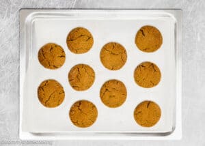 A baking tray with ten evenly spaced eggless gingersnap cookies rests on parchment paper.