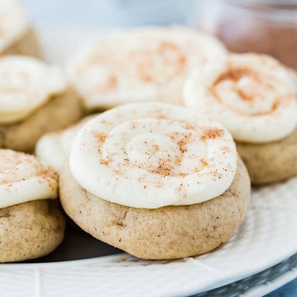 Close-up of eggless easy cinnamon roll cookies topped with white frosting and a sprinkle of spice, arranged on a plate.