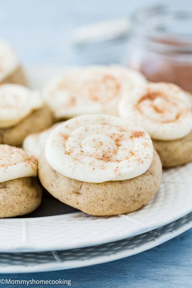 Close-up of eggless easy cinnamon roll cookies topped with white frosting and a sprinkle of spice, arranged on a plate.