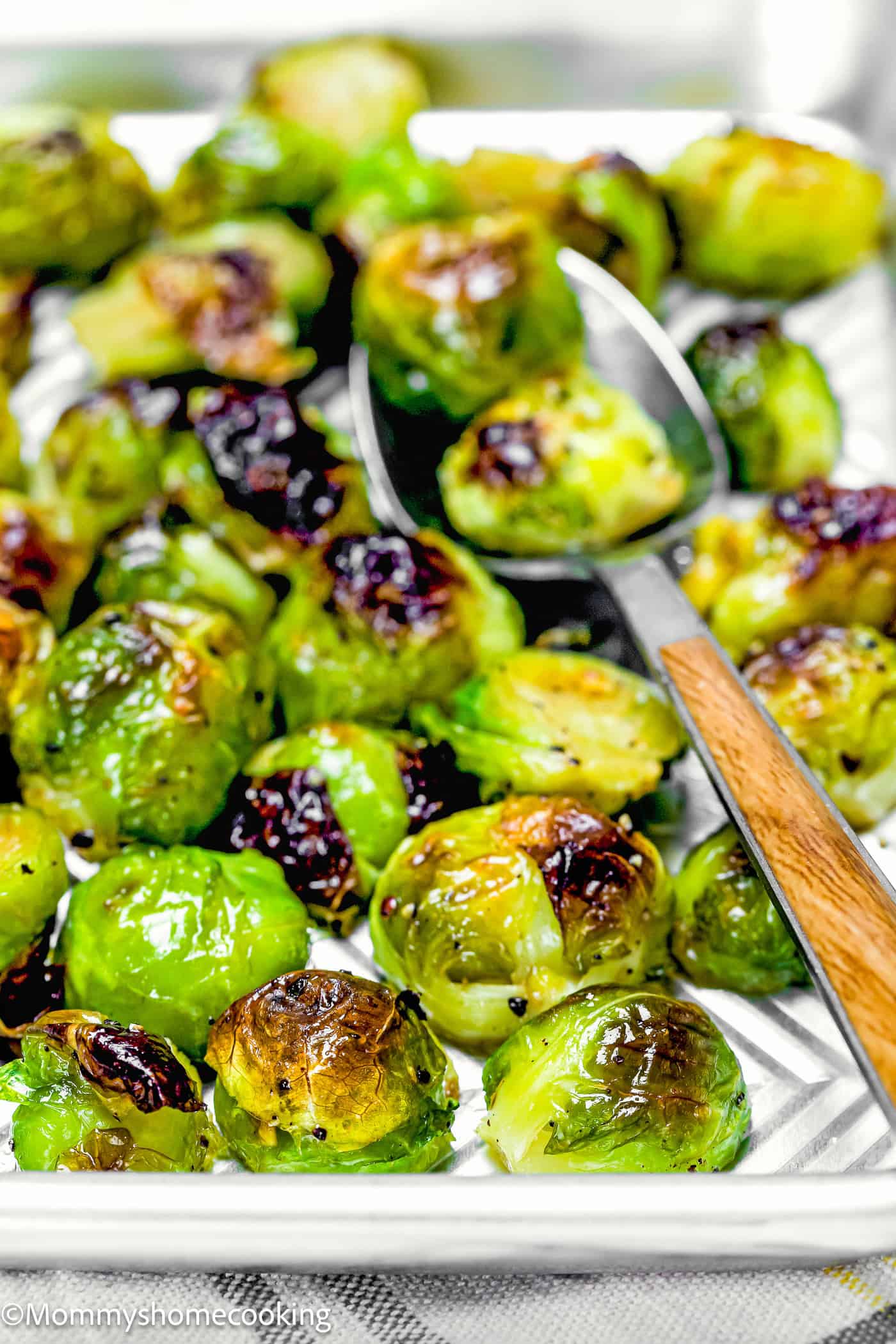 Easy Maple Roasted Brussels sprouts sit enticingly on a baking tray, their beautifully browned and crispy edges inviting attention. A metal spatula rests beside them, ready to serve this delightful dish.
