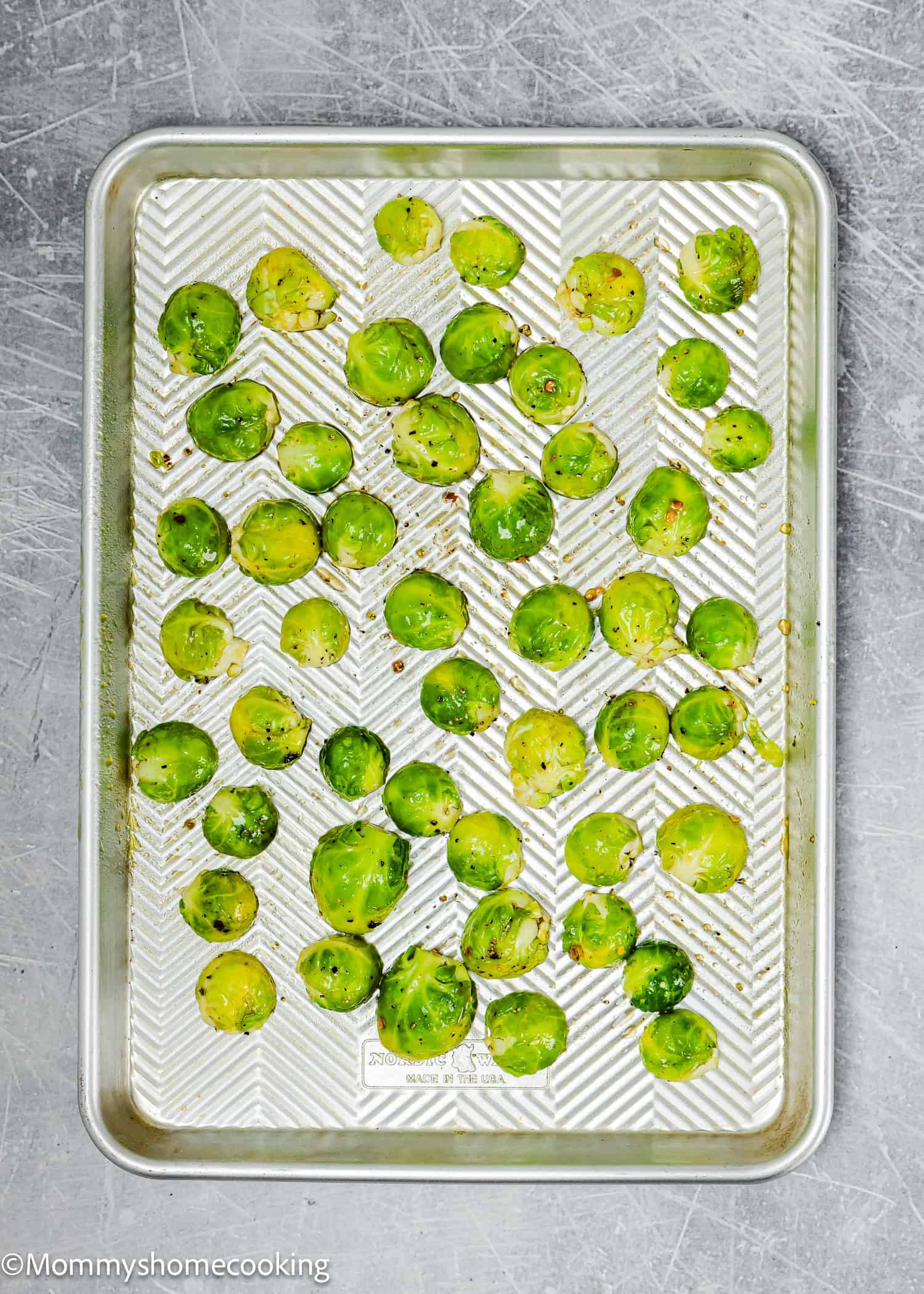 Easy maple-roasted Brussels sprouts halves are seasoned perfectly and arranged on a silver baking tray resting on a metallic surface.