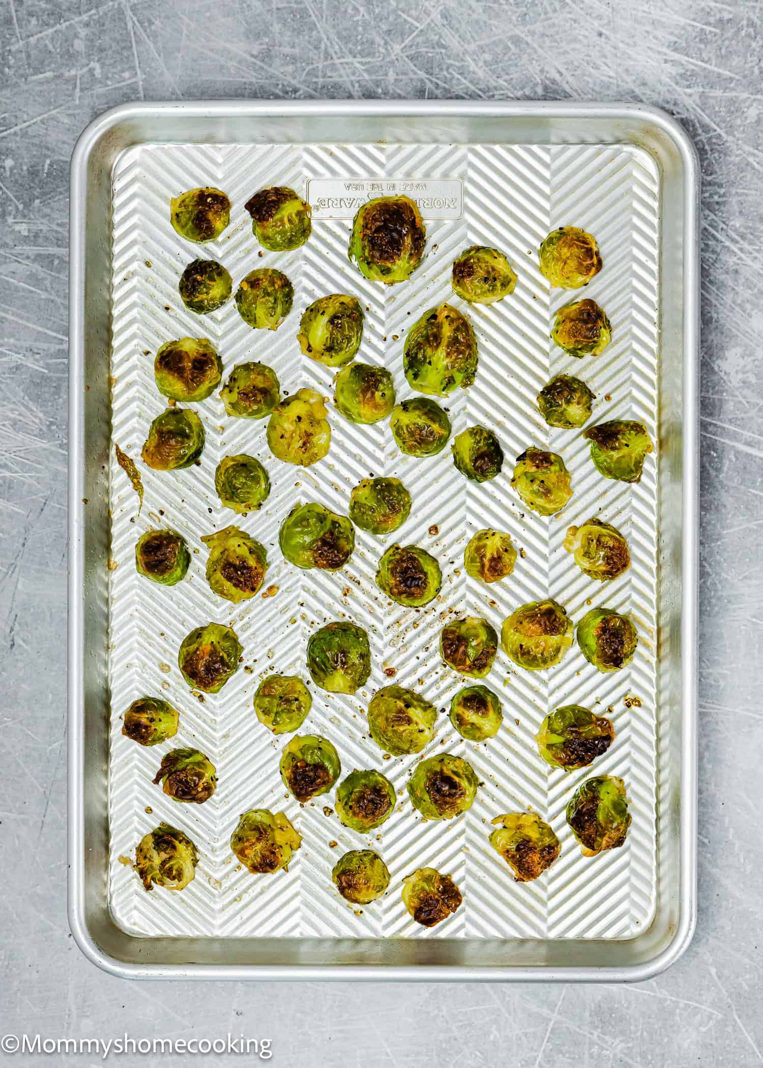 Easy maple-roasted Brussels sprouts scattered across a textured baking sheet, their golden edges caramelized to perfection.