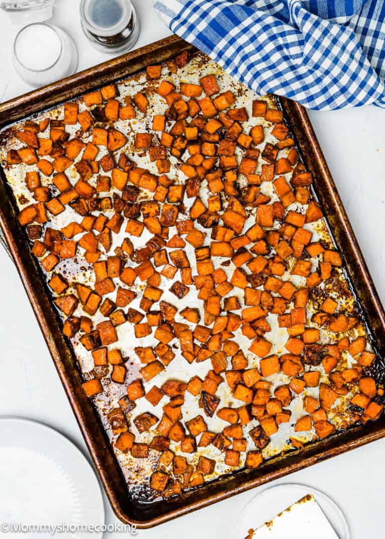 Easy Maple Roasted Sweet Potato cubes sit on a baking sheet, with a blue checkered cloth nearby, adding a touch of rustic charm.