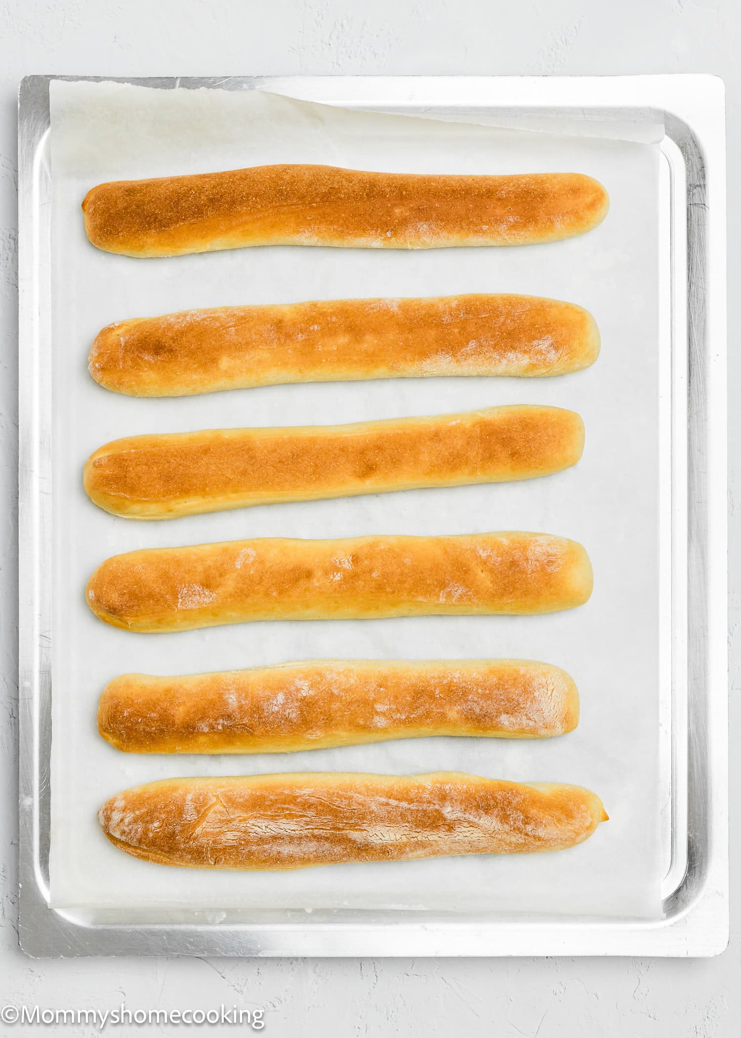 Six quick and easy breadsticks, both egg-free and dairy-free, are lined up in two rows on a baking sheet with parchment paper.