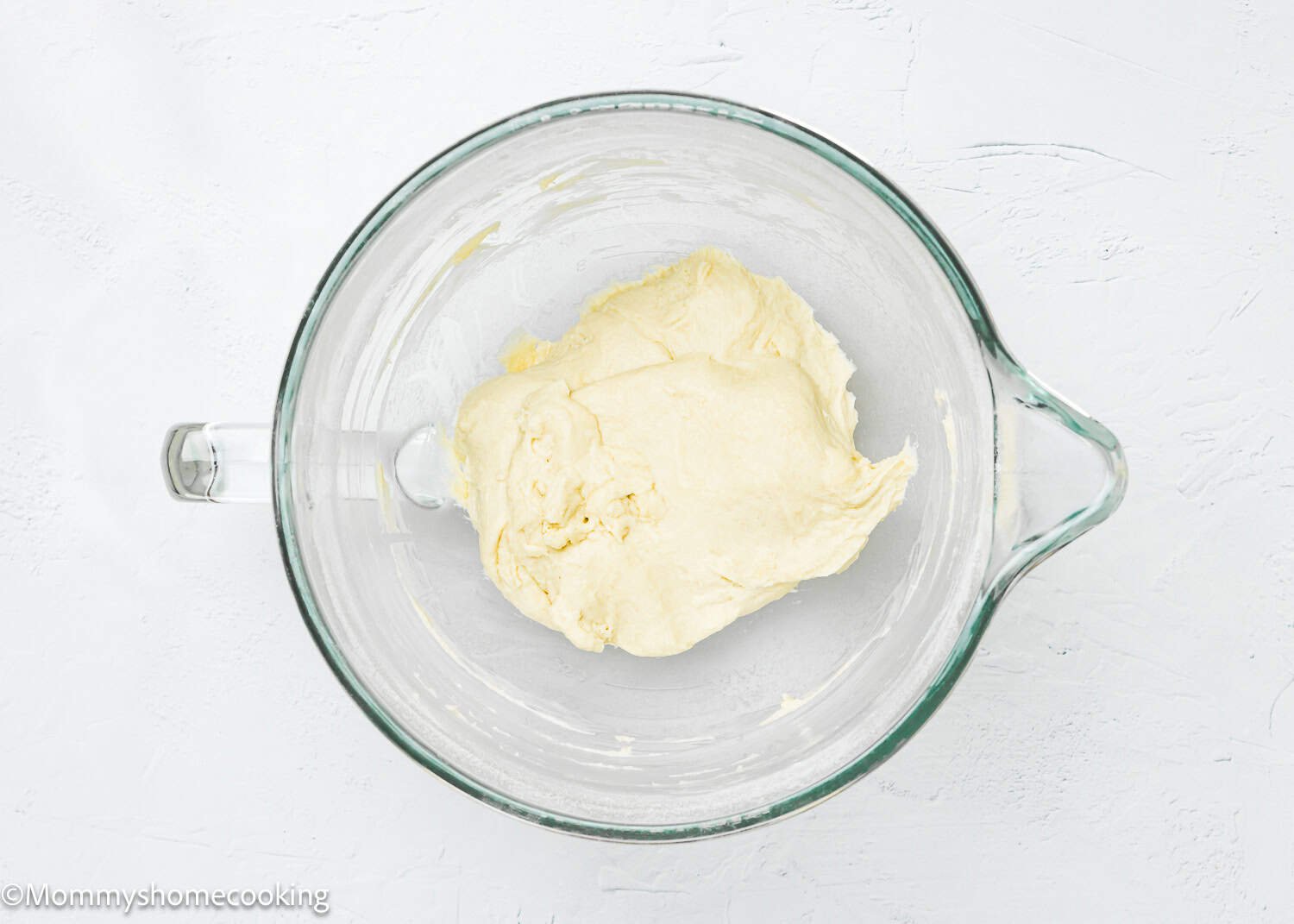 Quick and easy breadstick dough sits in a clear glass mixing bowl on a textured white surface, ready to become delicious egg-free and dairy-free treats.