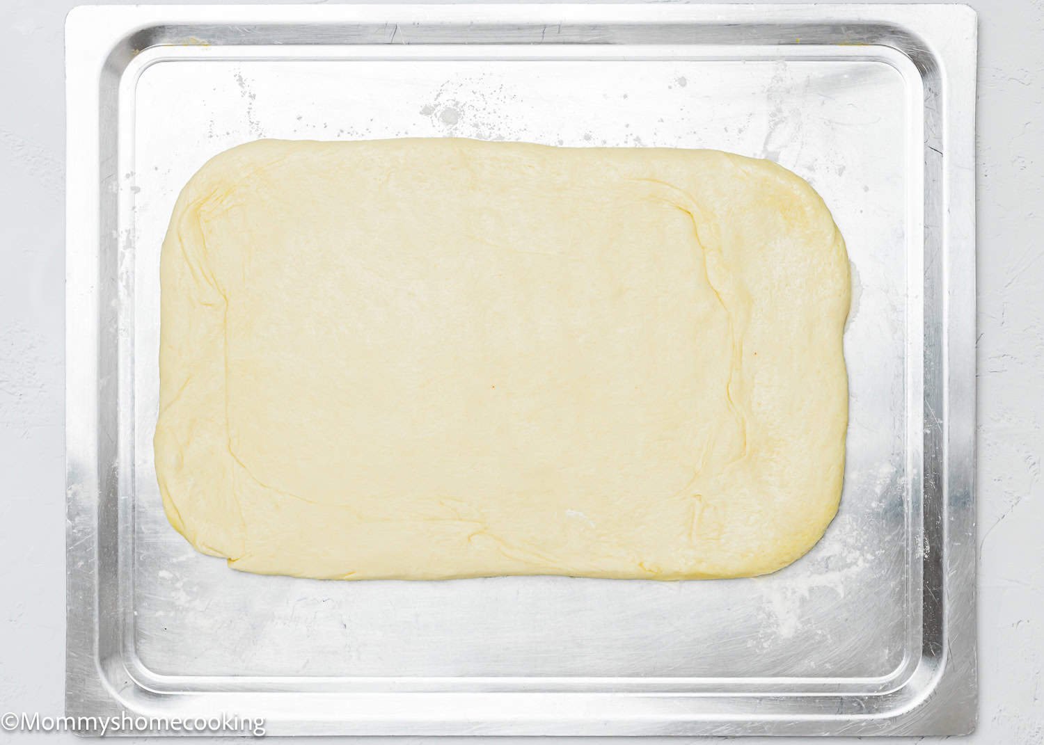 Quick and easy breadsticks, both egg-free and dairy-free, are ready for preparation as dough is rolled out flat on a metal baking sheet.