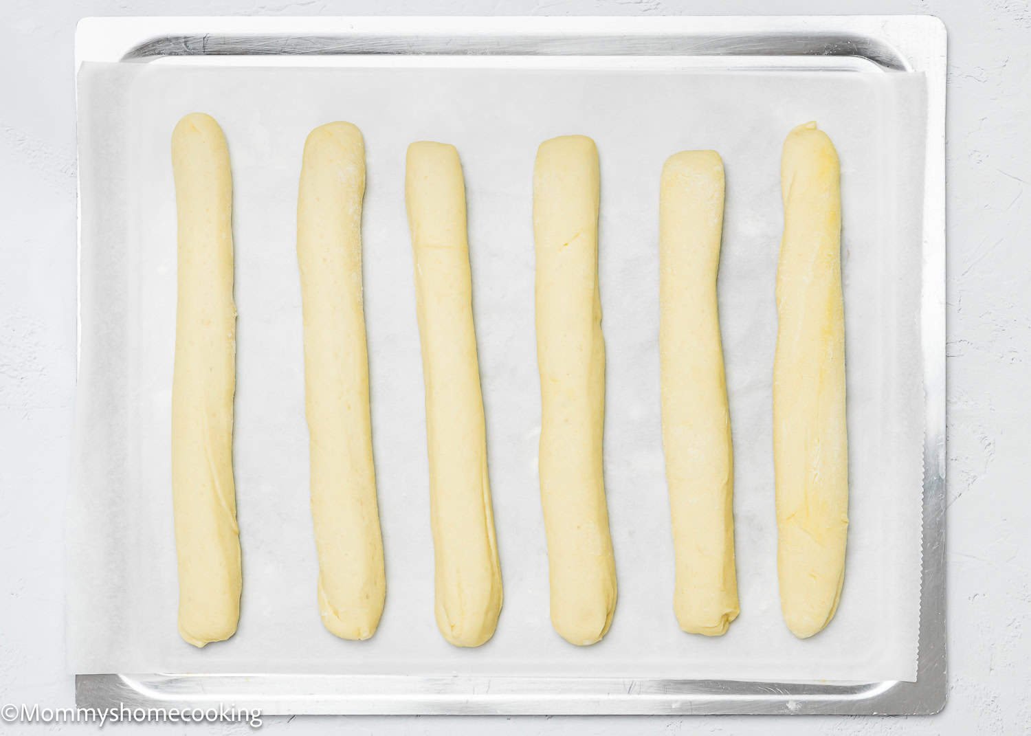Six quick and easy breadsticks, egg-free and dairy-free, are evenly spaced on a parchment-lined baking sheet.