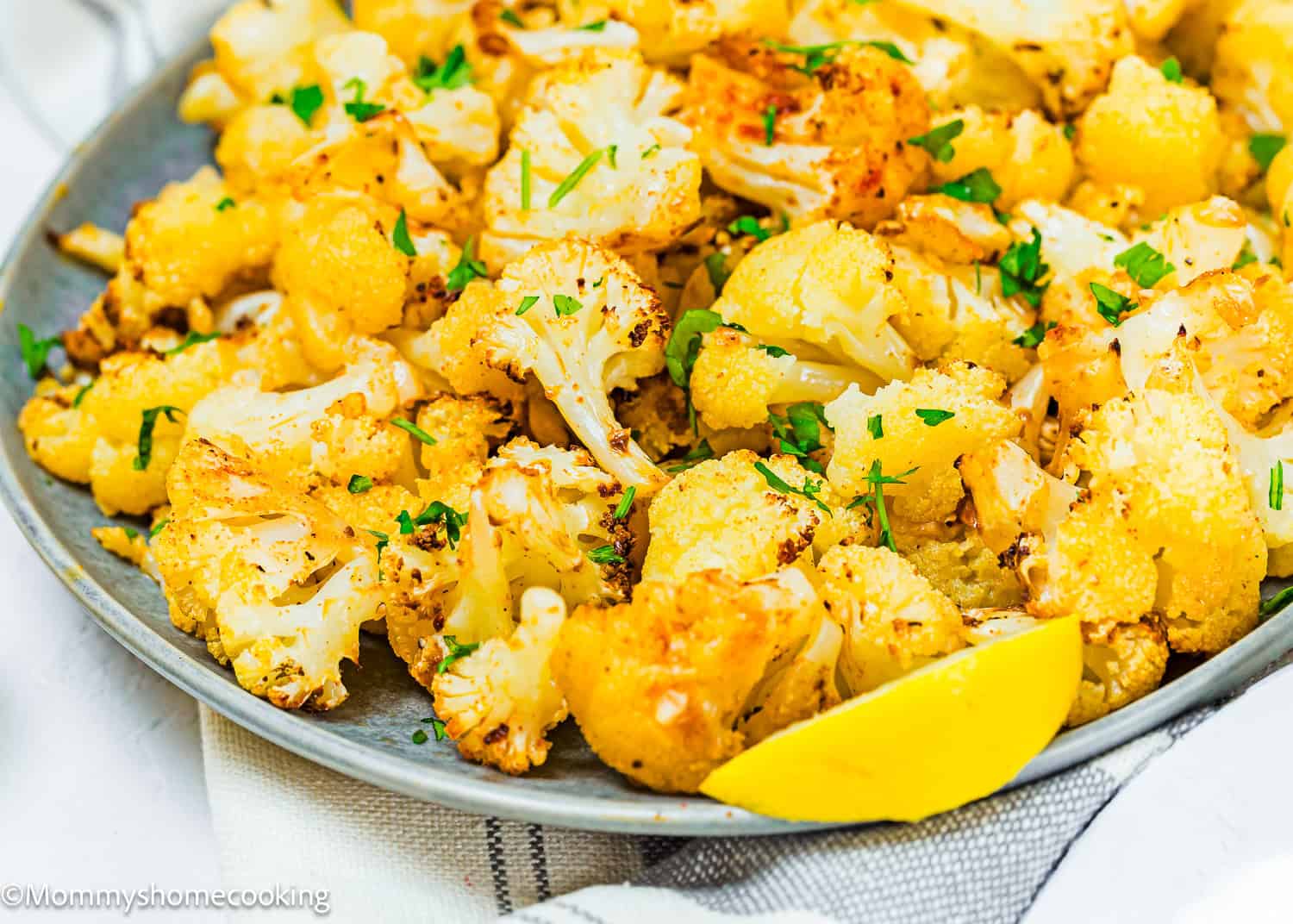 A quick and easy plate of roasted cauliflower florets, perfectly garnished with chopped herbs and served with a refreshing lemon wedge.