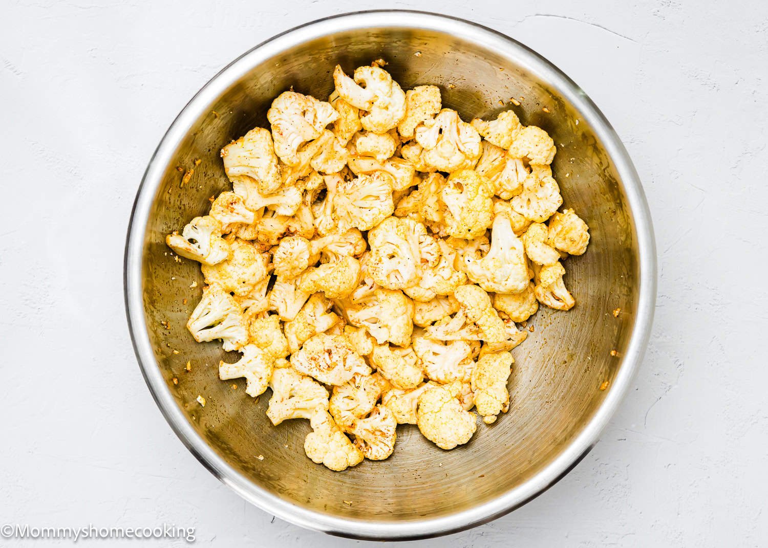 A large metal bowl holds cauliflower florets, perfectly seasoned.