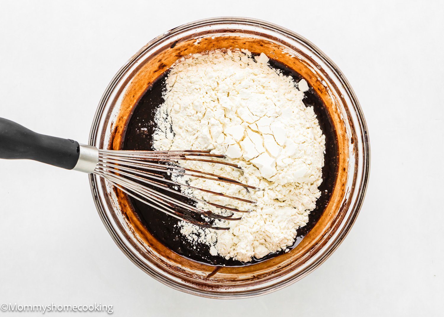 A glass bowl contains wet ingredients to make the best eggless brookies.