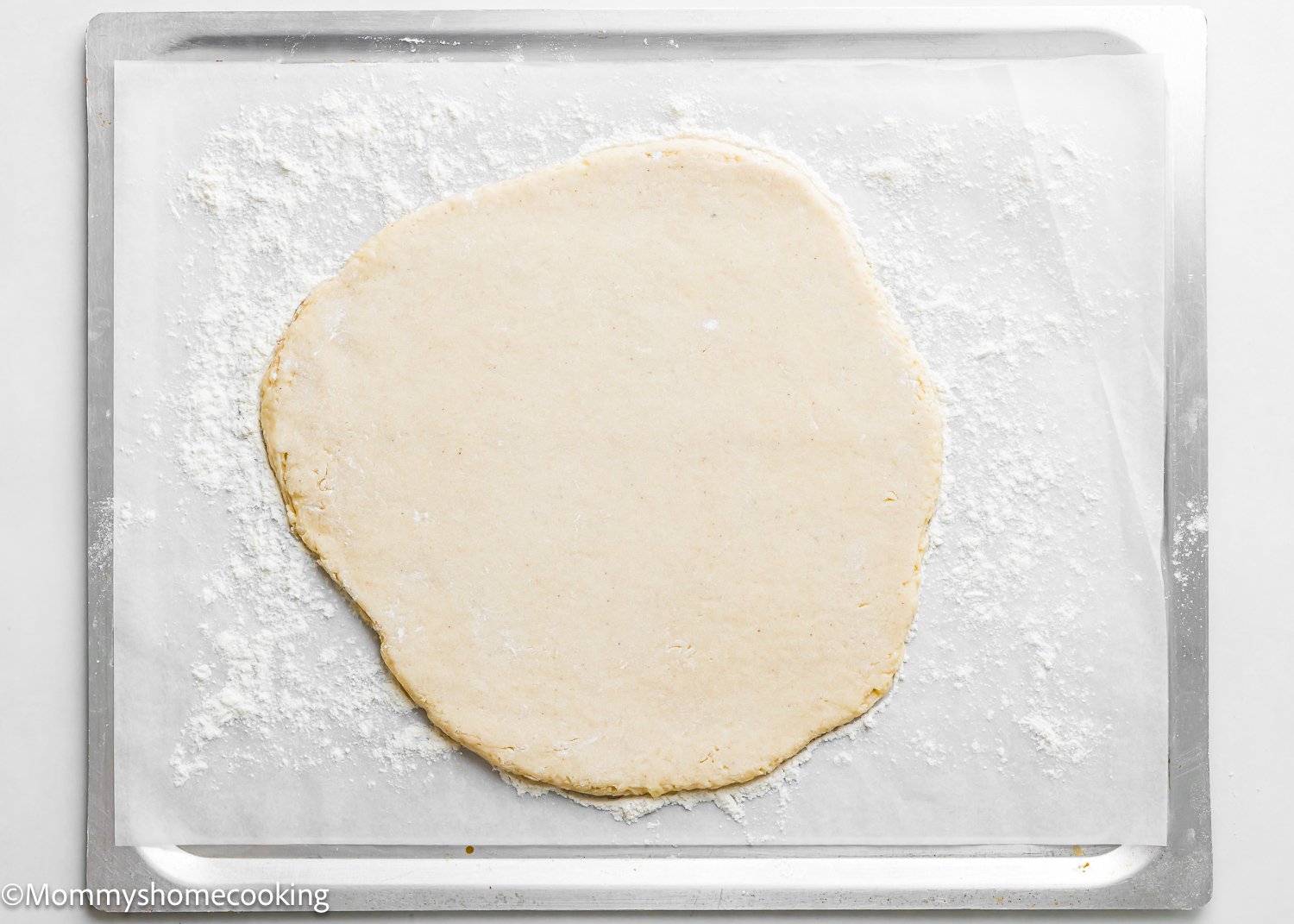 Dough rolled out in a rough circle shape on parchment paper atop a floured baking sheet, just like prepping for the best eggless cake donuts, quick and easy.