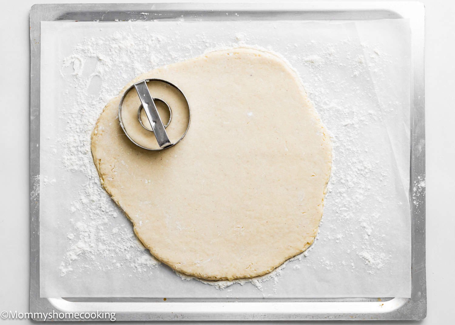 Dough rolled out on a floured baking sheet with a round cutter placed on top, perfect for crafting the best eggless cake donuts that are quick and easy to make.