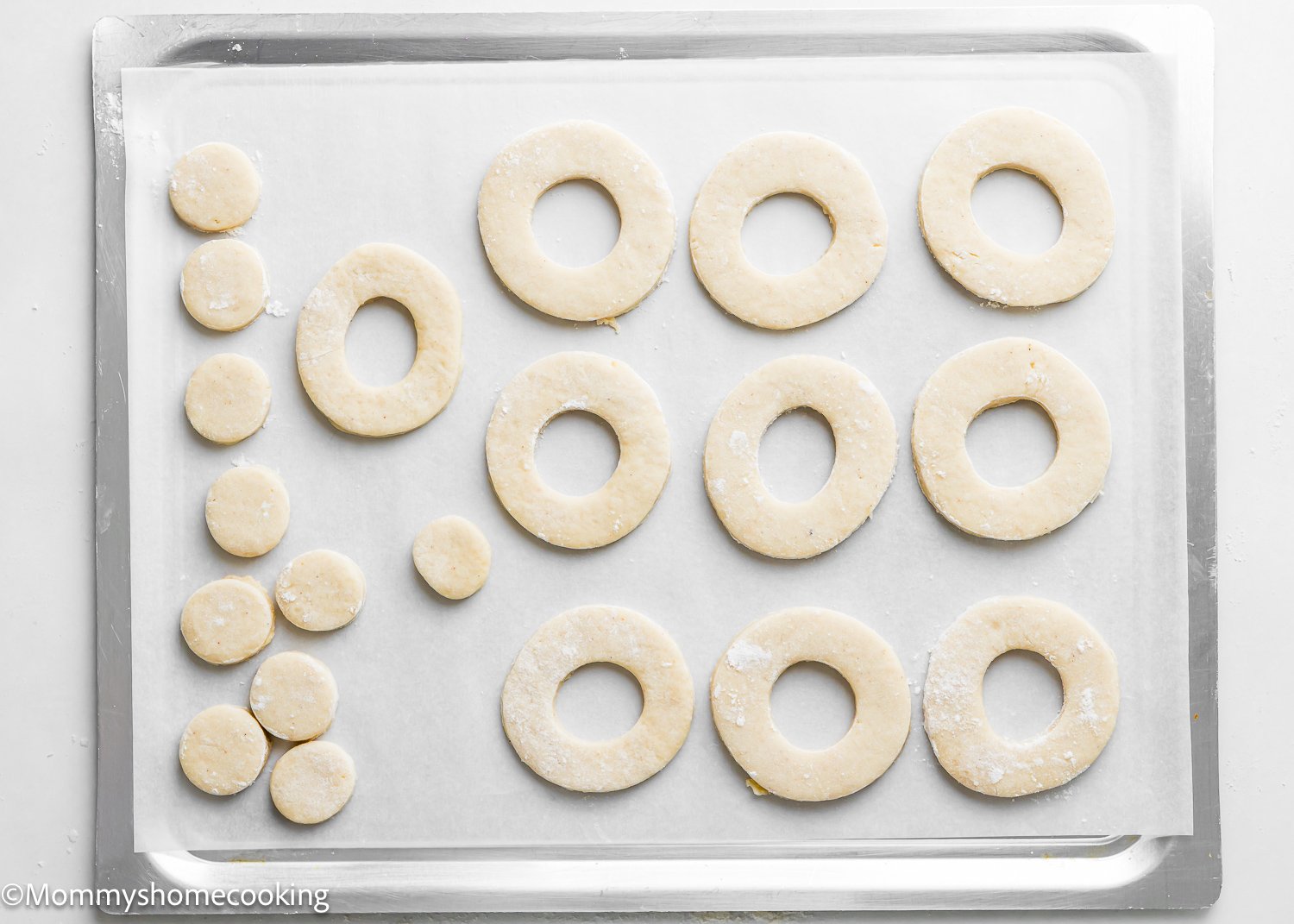 Dough rings and small circular cutouts arranged on a parchment-lined baking sheet, these best eggless cake donuts are quick and easy to prepare, ready for baking perfection.