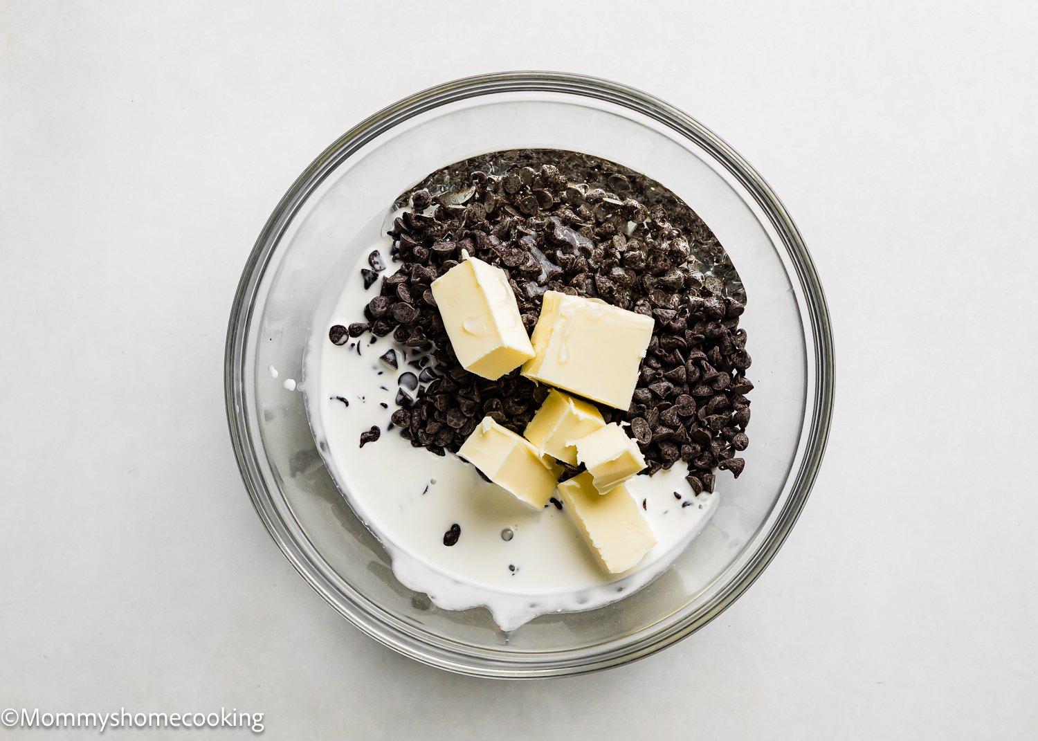 A bowl filled with chocolate chips, chopped chocolate, butter, and cream awaits melting, perfect ingredients for creating a rich glaze for your Chocolate Frosted Cake Donuts (Egg-Free).