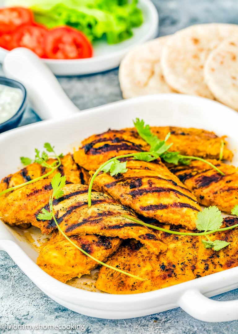 Easy Chicken Shawarma: Succulent grilled chicken pieces garnished with cilantro in a white dish, accompanied by sliced tomatoes, crisp lettuce, pita bread, and a flavorful dip in the background.