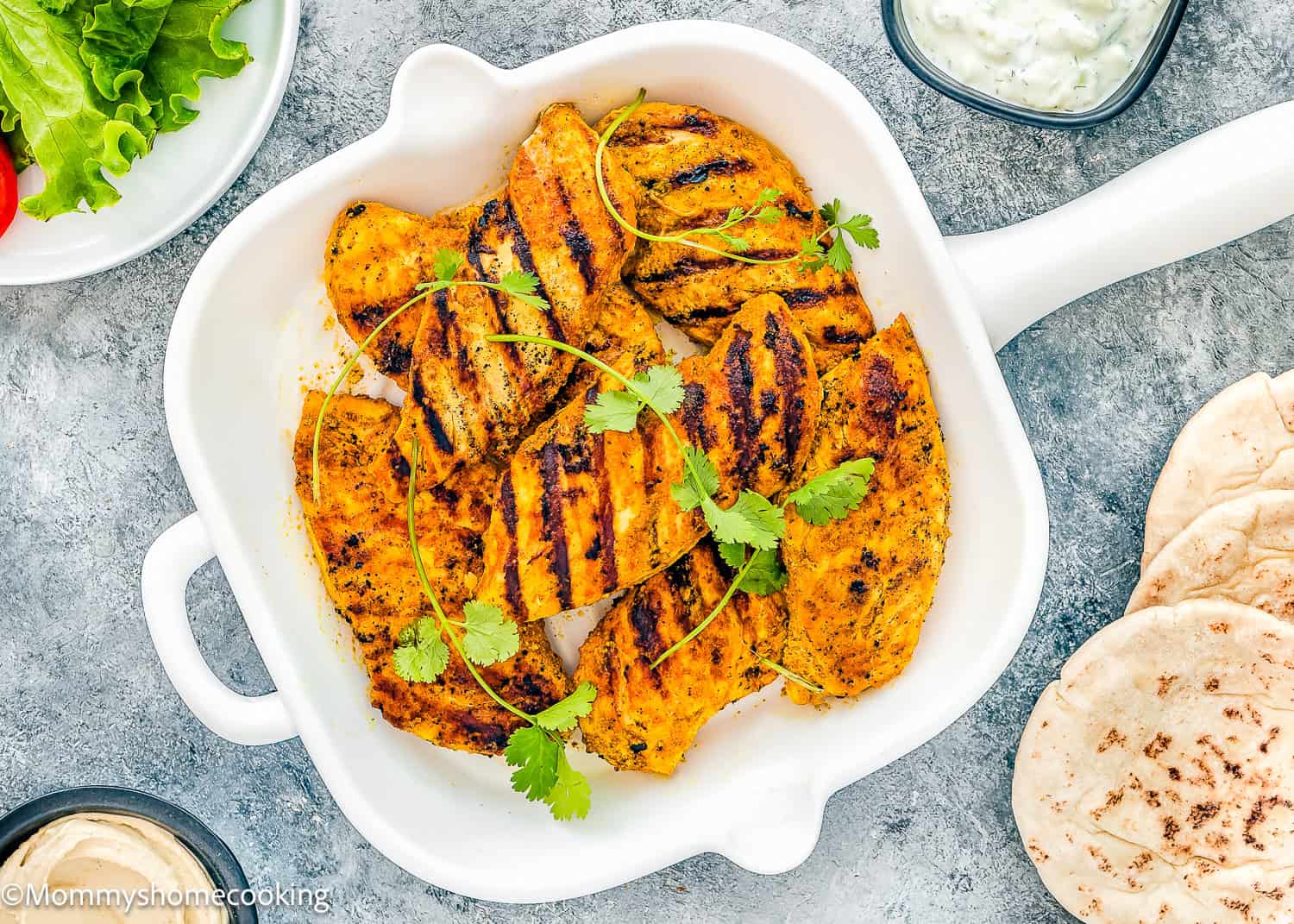 Easy Chicken Shawarma served in a white dish, featuring succulent grilled chicken pieces garnished with cilantro. Accompanied by warm pita bread and a flavorful bowl of sauce, this dish brings together the essence of delightful Middle Eastern cuisine effortlessly.