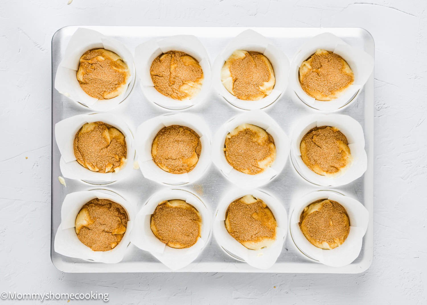 A baking tray with twelve muffin cups, each filled with luscious eggless coffee cake batter and lined with white paper.