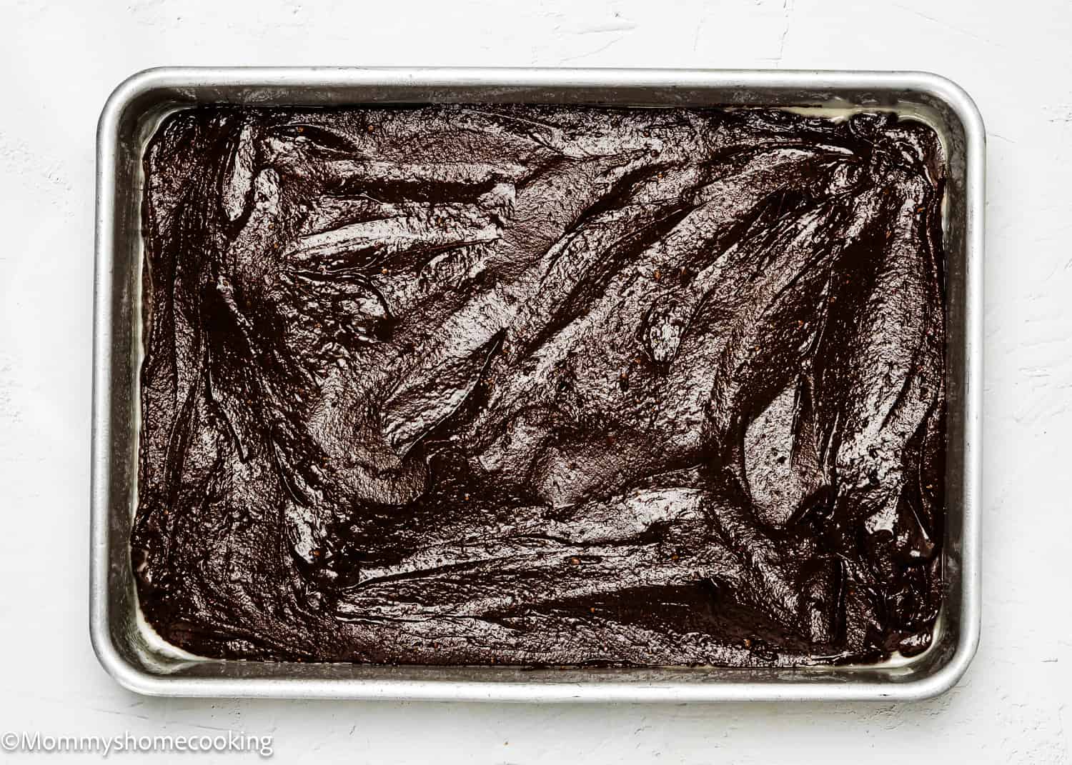 The baking tray is filled with thick, dark chocolate brownie batter, creating an inviting canvas for a delightful eggless red velvet brownie poke cake masterpiece.