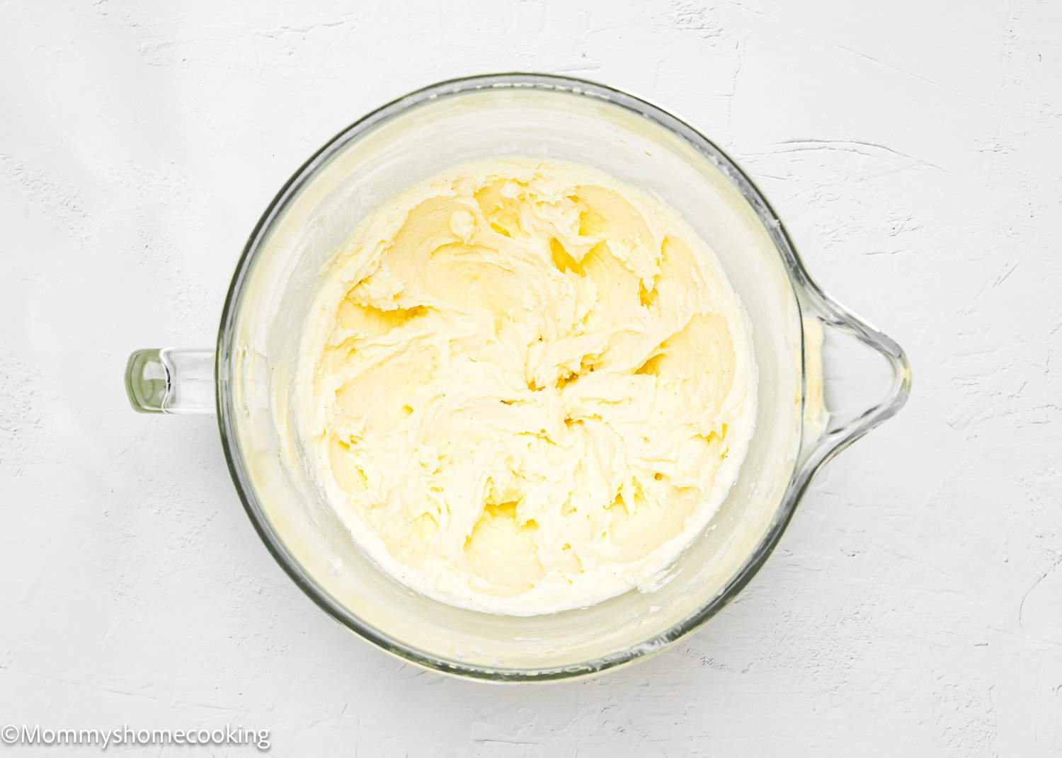 A glass bowl filled with creamy, whipped butter sits on a white textured surface, ready to add a touch of indulgence to your eggless Valentine's striped sugar cookies.