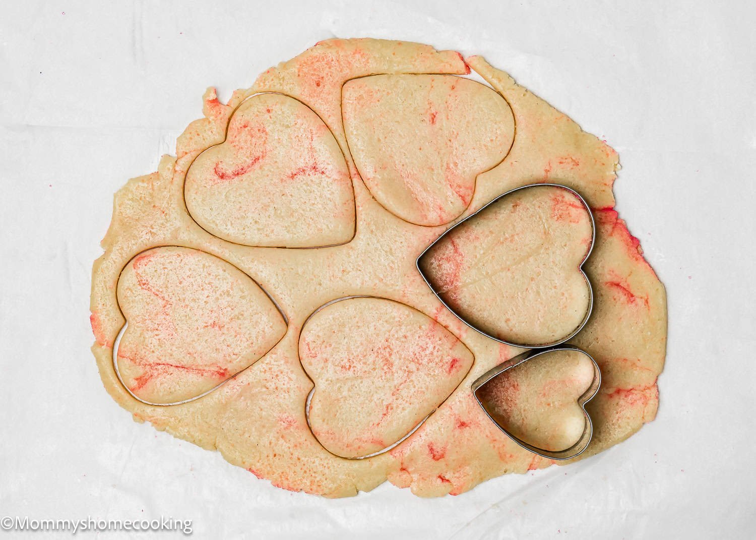 Eggless Valentine's striped sugar cookies come to life as heart-shaped cutters press into rolled-out dough with vibrant red streaks.