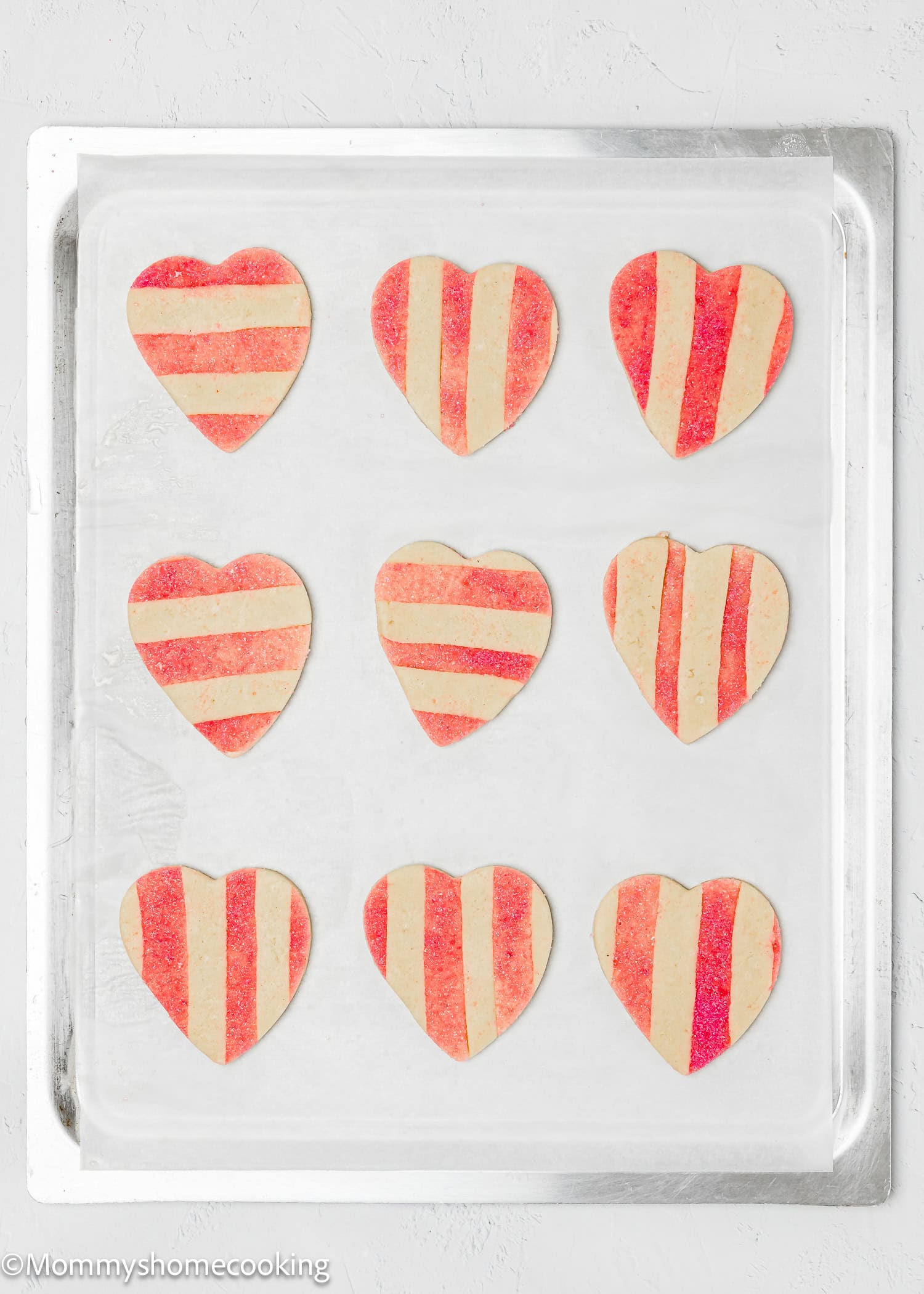 Nine Eggless Valentine's striped sugar cookies with red and beige patterns are arranged in a 3x3 grid on a baking sheet.