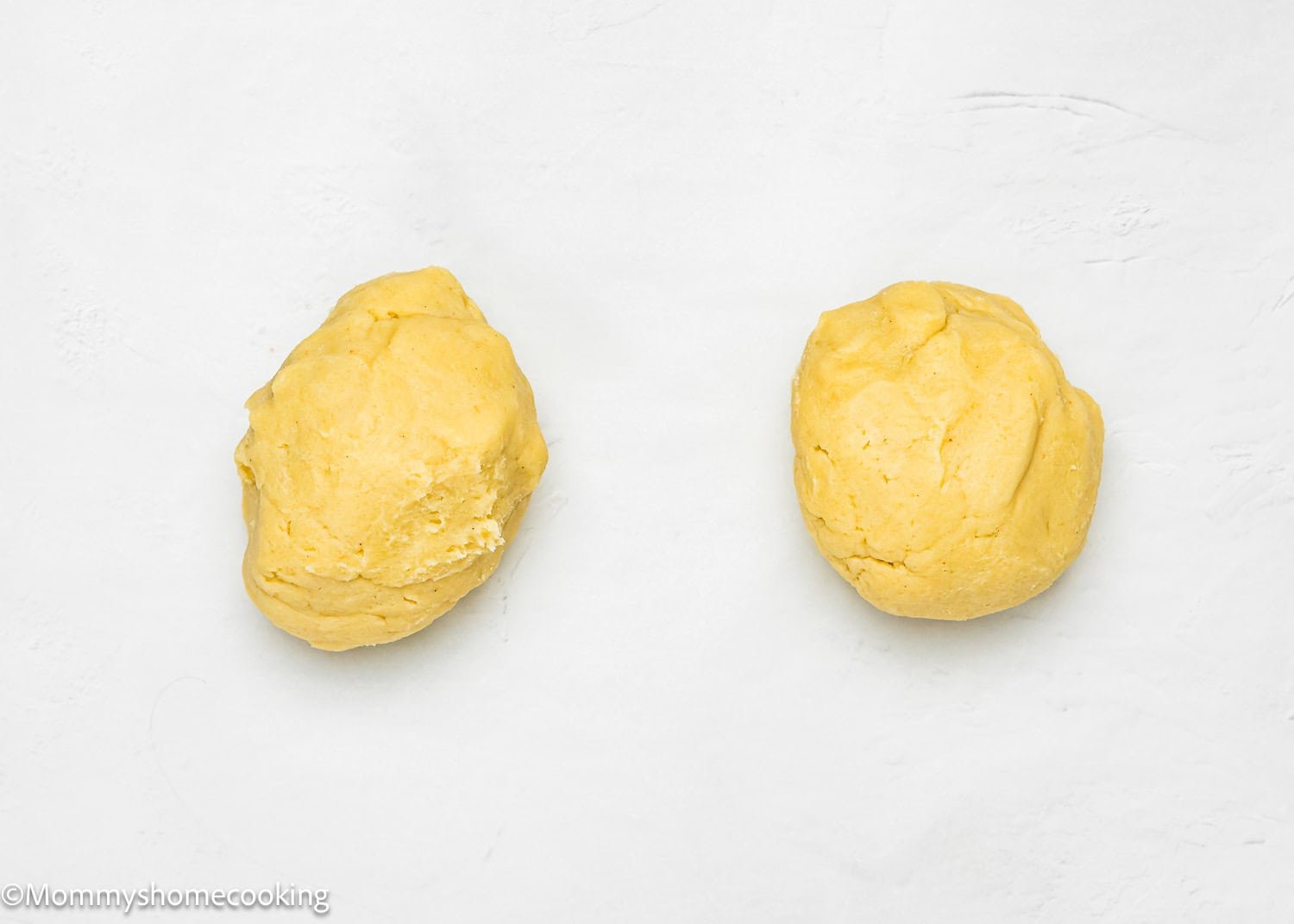 Two portions of yellow dough, destined to become eggless Valentine's striped sugar cookies, rest side by side on a pristine white surface.