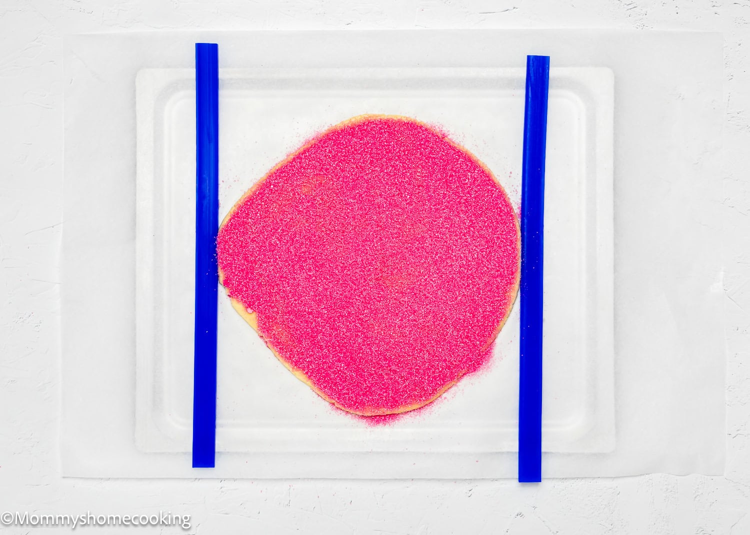 A flat circle of pink sprinkles rests between two blue strips on a white surface, resembling the whimsical charm of eggless Valentine's striped sugar cookies.