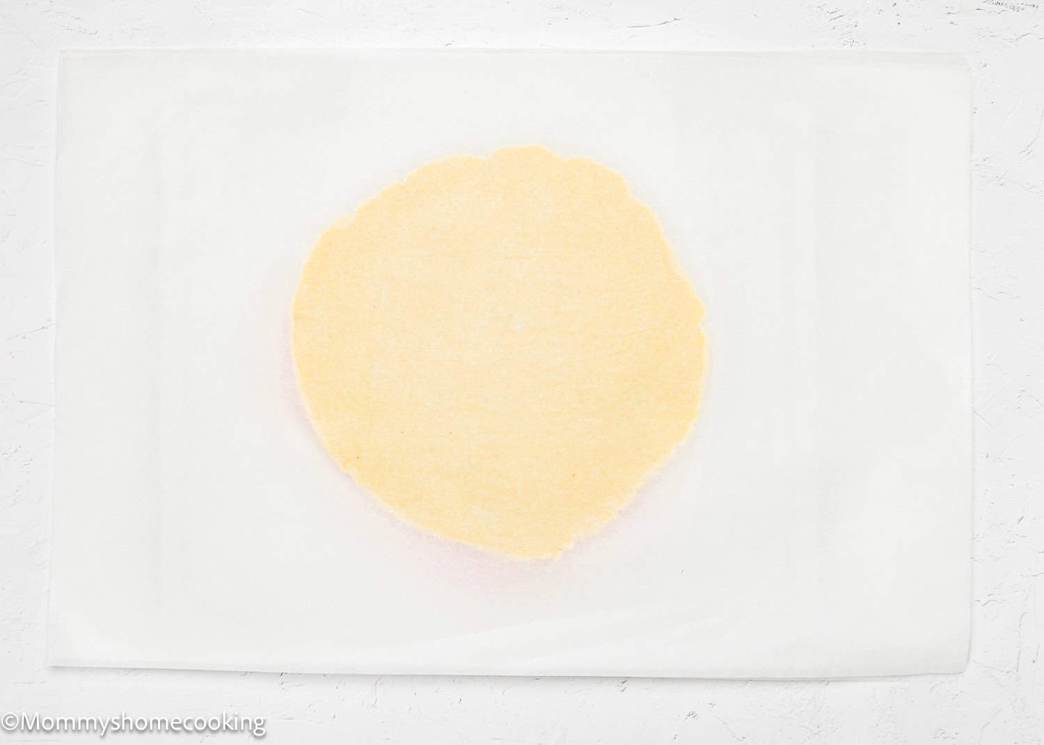 A round, uncooked dough for eggless Valentine's striped sugar cookies rests on a sheet of parchment paper on a white surface.
