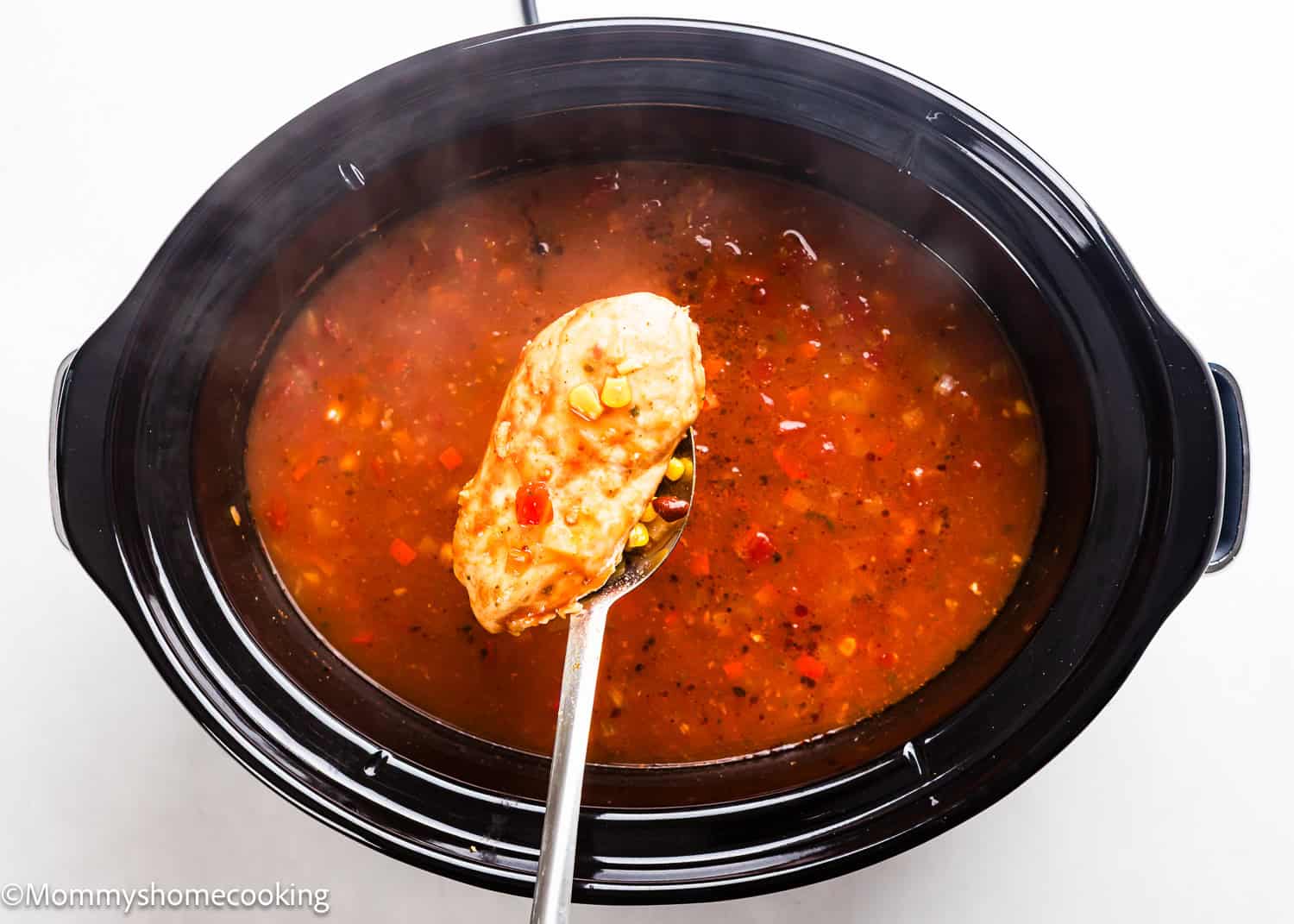 A slow cooker filled with vibrant chicken tortilla soup, featuring corn and vegetables, with a ladle holding a scoop of the delicious blend above it.