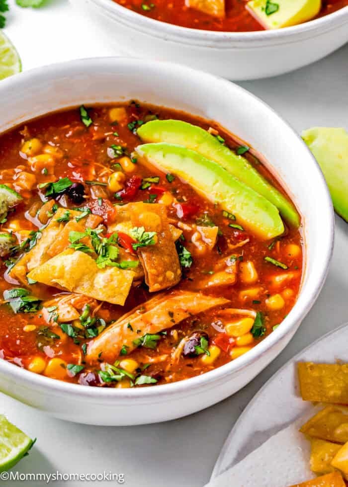 A delicious bowl of slow cooker chicken tortilla soup, topped with fresh avocado slices, crunchy tortilla strips, sweet corn, black beans, and chopped cilantro.