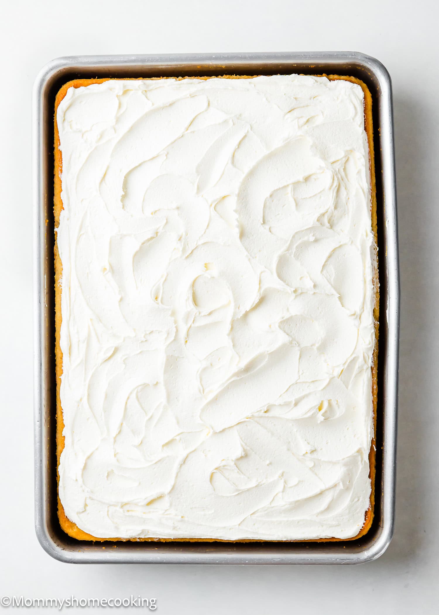 An easy, rectangular sheet cake with white frosting rests in a metal pan on a white background. This egg-free and dairy-free vanilla sheet cake is perfect for any occasion.