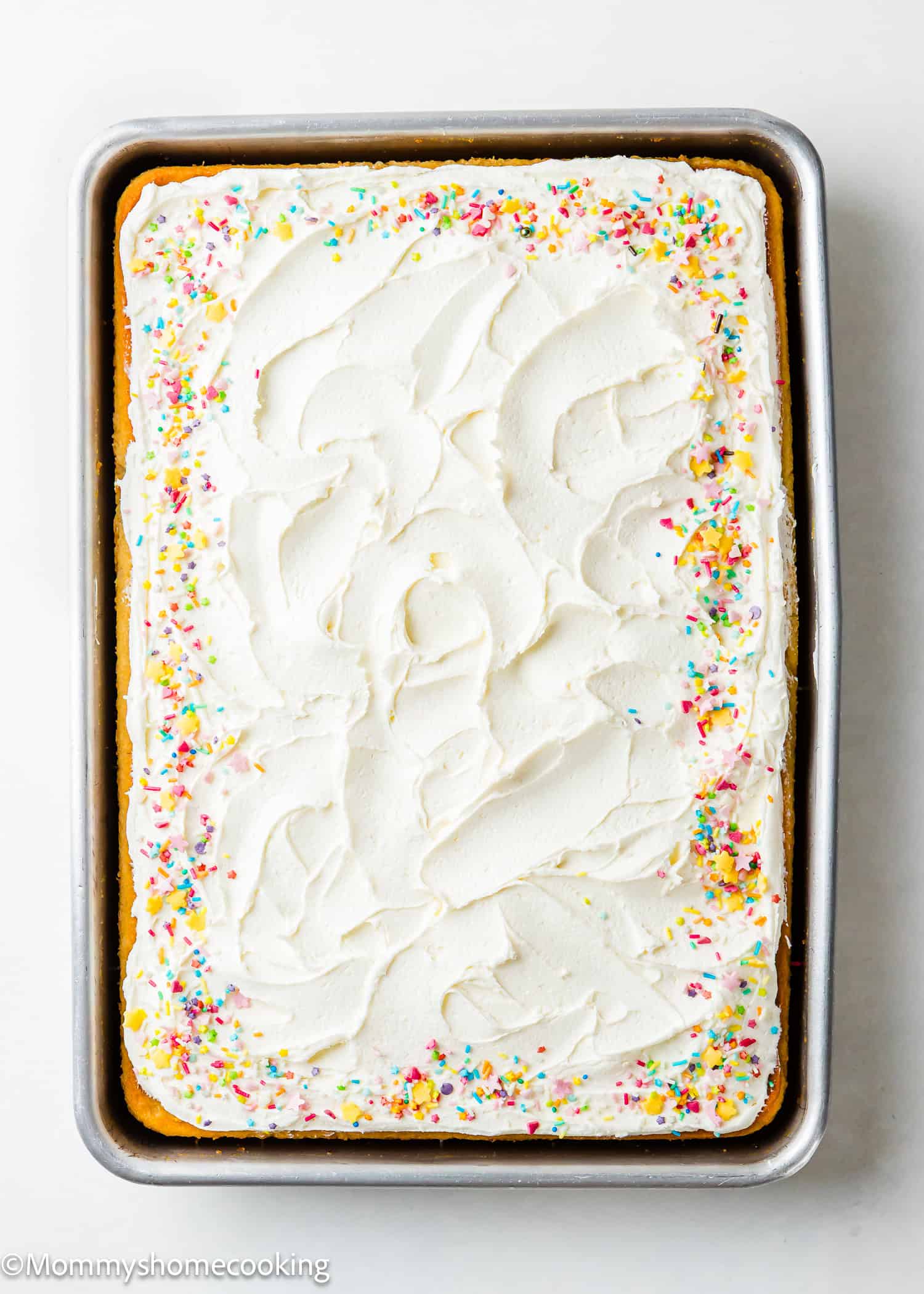 This easy, rectangular vanilla sheet cake boasts white frosting and colorful sprinkles in a metal baking pan. Egg-free and dairy-free, it's perfect for any occasion.