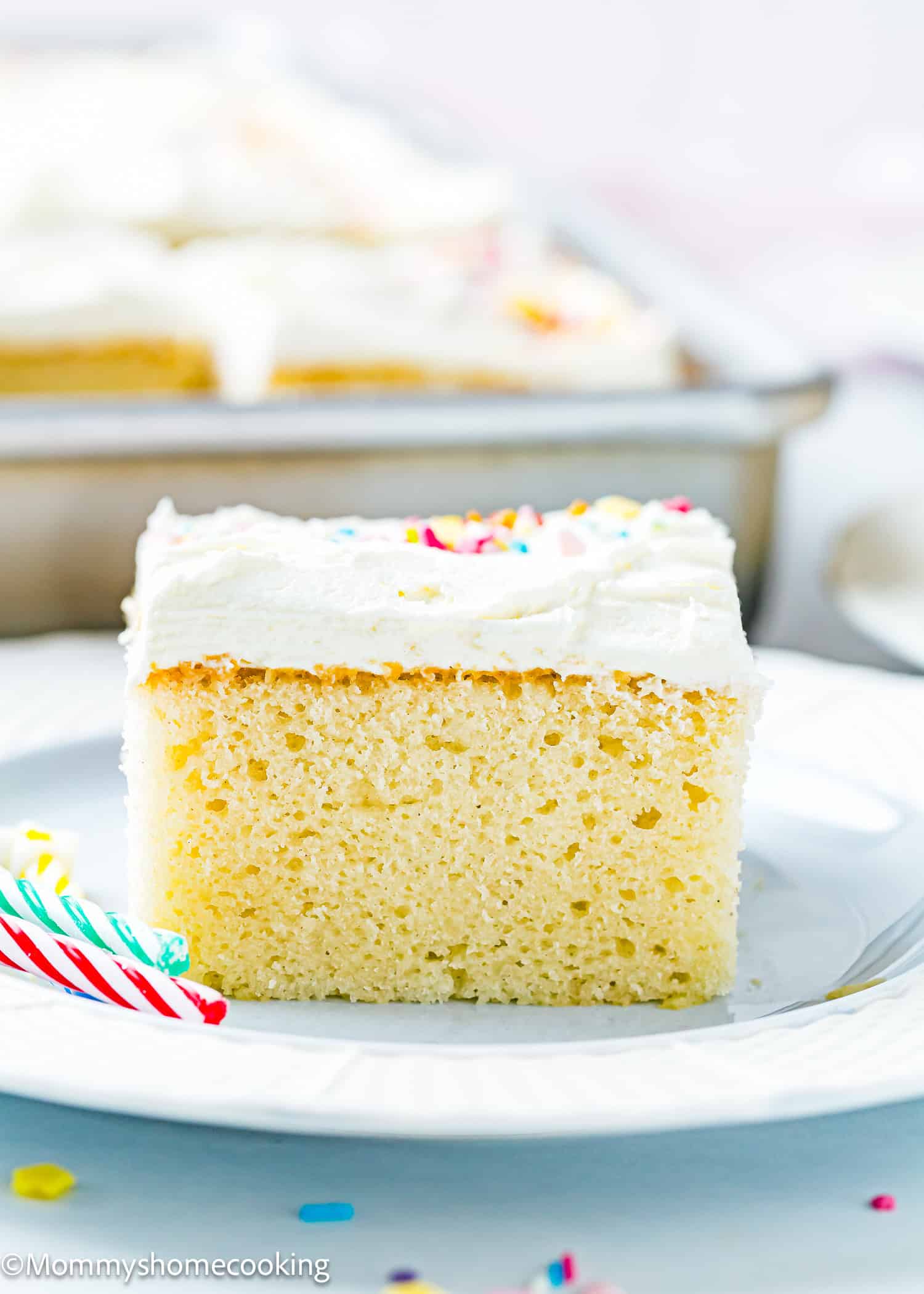 An easy slice of egg-free and dairy-free vanilla sheet cake with white frosting and colorful sprinkles sits on a white plate, with a fork nearby.