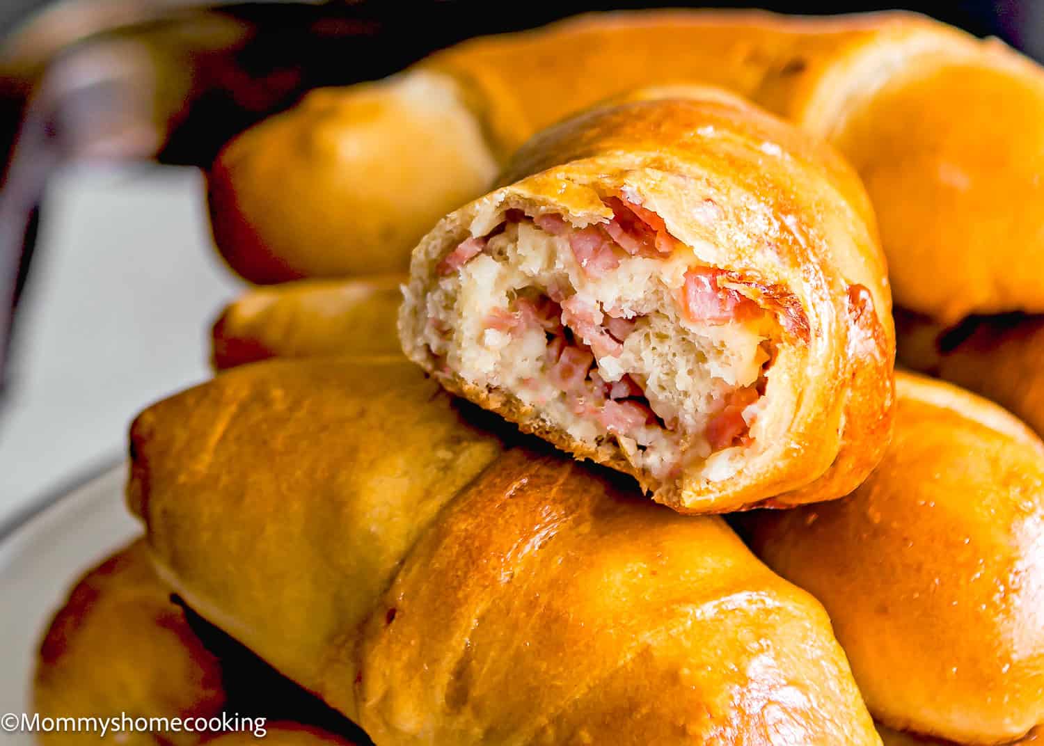 A plate of golden-brown Venezuelan Cachitos , with one on top revealing a savory filling of chopped ham.