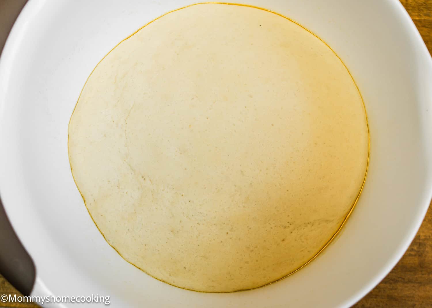 A bowl with dough rising, showing a smooth, round surface, hints at the irresistible allure of Venezuelan Cachitos de Jamon as the dough has been proofed to perfection.