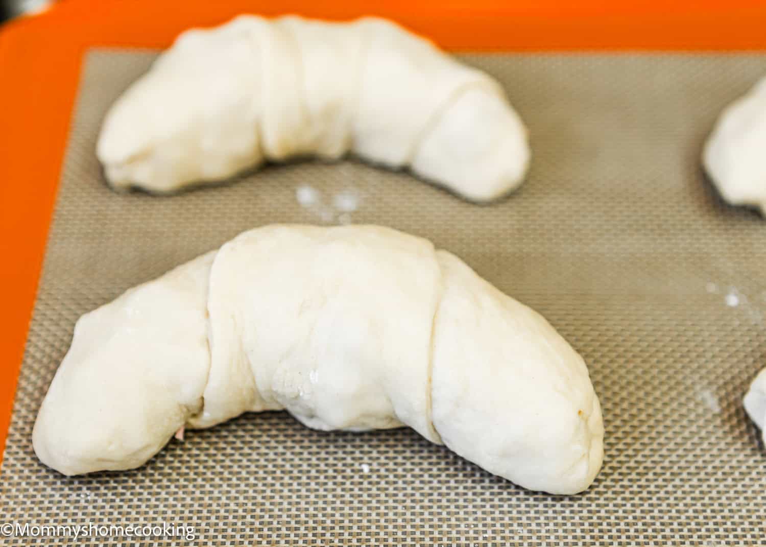 Unbaked Venezuelan cachitos de jamon placed on a baking sheet lined with a silicone mat.