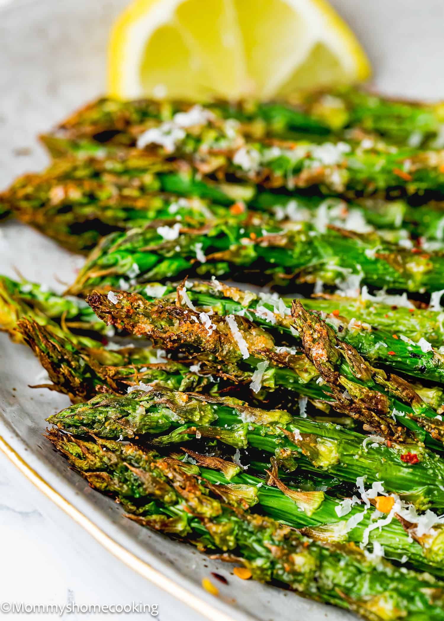 Grilled asparagus spears topped with grated cheese and seasoning are presented on a white plate, garnished with a lemon wedge. Discover the art of perfect Air Fryer asparagus in every crisp bite.