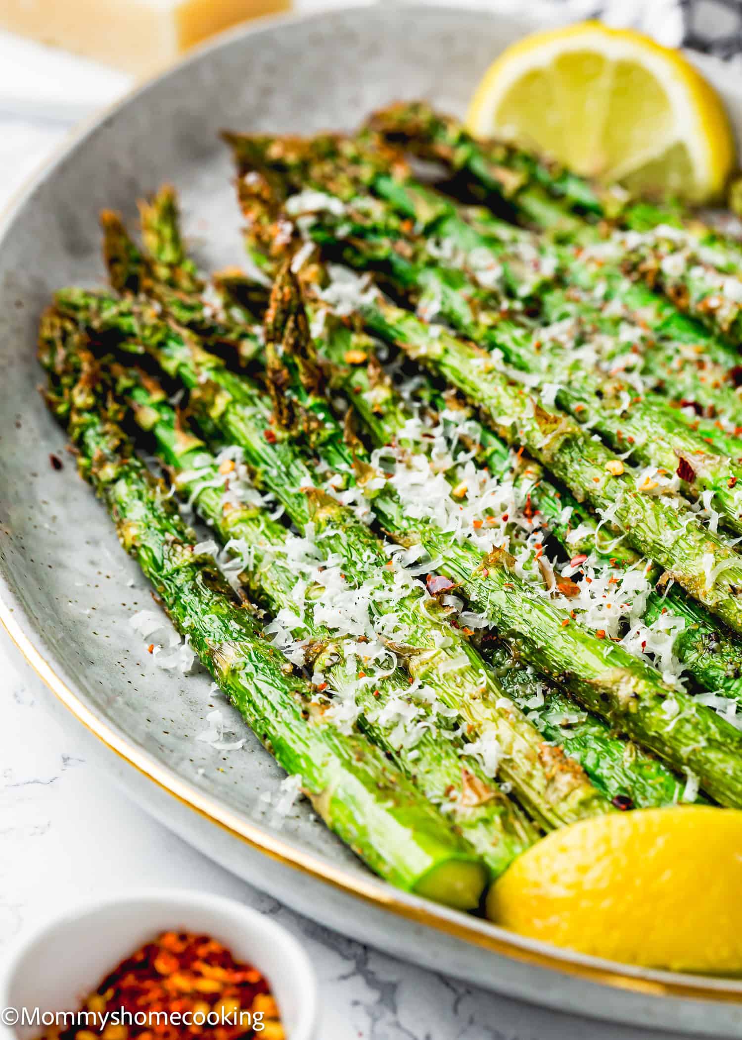 A plate of perfect air fryer asparagus topped with grated cheese and red pepper flakes, garnished with lemon wedges.