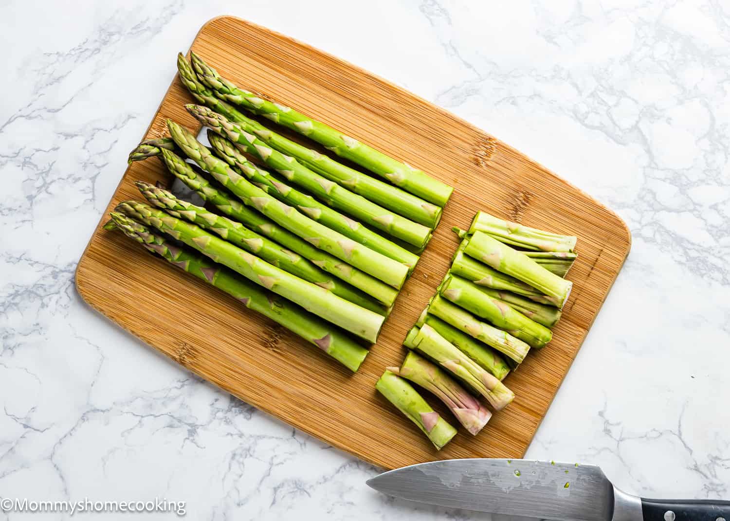 Fresh asparagus spears, trimmed to perfection, lie on a wooden cutting board beside a knife, ready to be transformed into perfect Air Fryer Asparagus on the marble countertop.