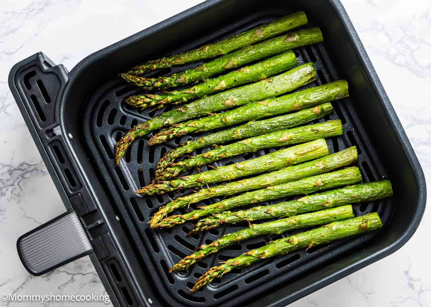 Freshly cooked, perfect air fryer asparagus rests inside an air fryer basket, elegantly set on a marble countertop.