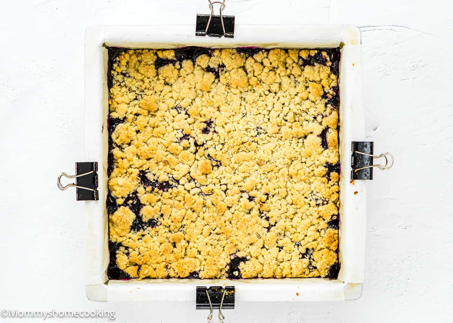 A square baking pan holds Easy Eggless Blueberry Oat Crumb Bars, featuring a crumbly golden topping over a dark berry filling.