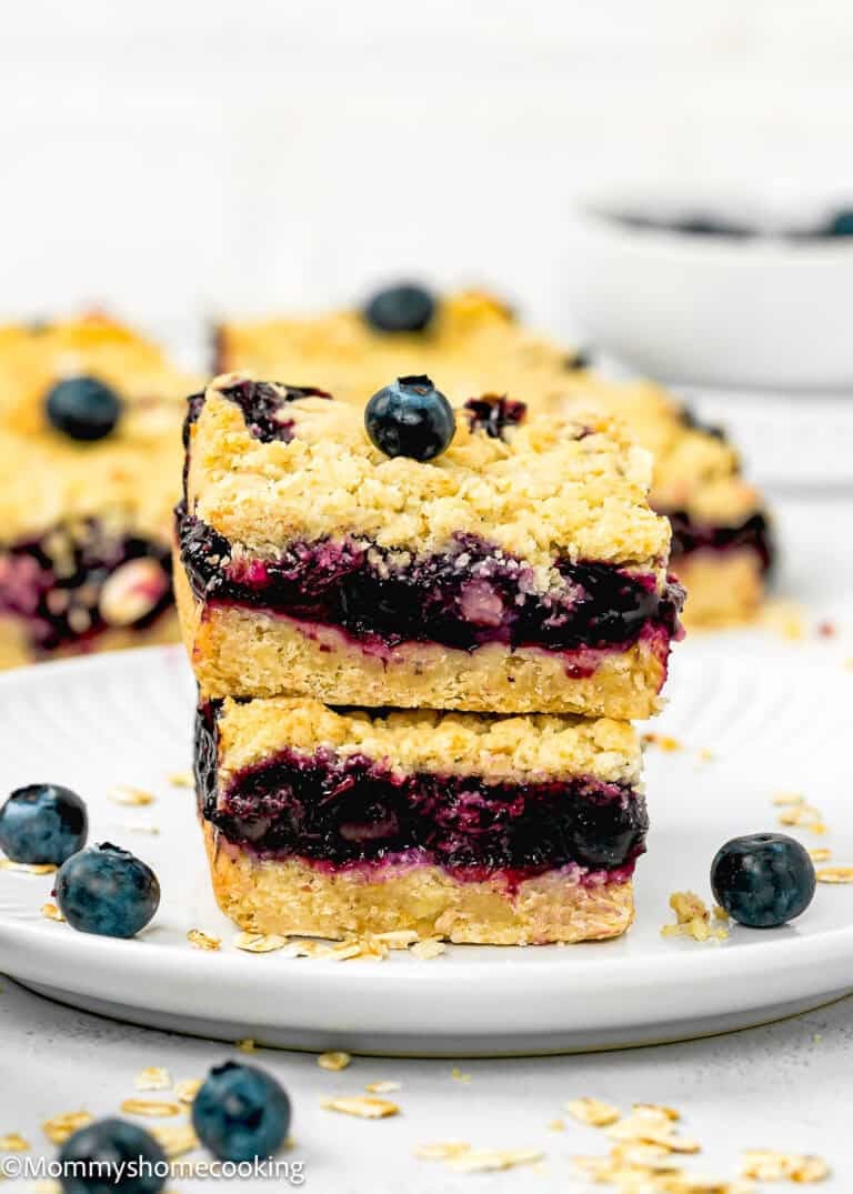 Two easy, eggless blueberry oat crumb bars stacked on a white plate, with oats and fresh blueberries scattered around.